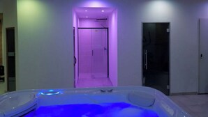 A modern spa room with a hot tub, a shower area, and a door leading to another room.