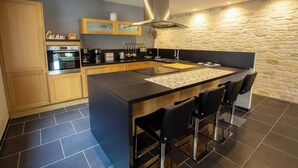 A modern kitchen with a central island, bar stools, a built-in oven, and a stone wall backsplash.
