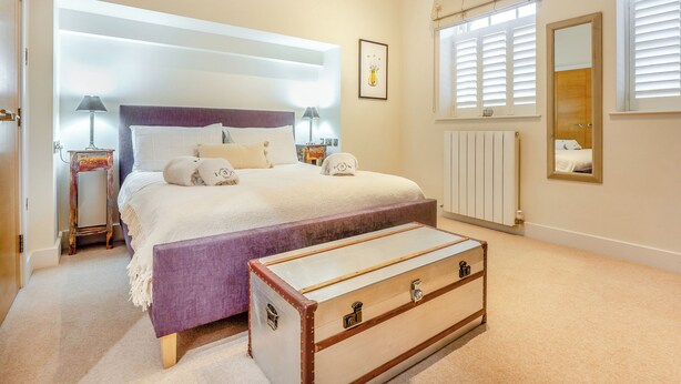 Quarto com cama, luminárias de cabeceira, cômoda, radiador e janela com persianas.