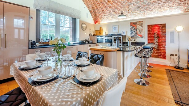 Un comedor con techo de ladrillo, una cocina al fondo y una mesa puesta con vajilla blanca.