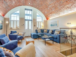 A living room with a brick ceiling, a large window, a blue sofa set, and a glass coffee table.