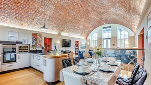 Uma cozinha espaçosa com eletrodomésticos modernos, uma área de jantar com uma mesa redonda e cadeiras, e uma sala de estar com sofá e televisão.