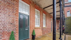 Um edifício de tijolos com porta verde, janelas brancas e entrada pavimentada.