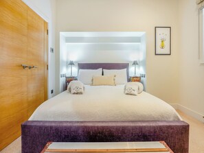 A neatly made bed with two pillows, a bedside table with a lamp, and a framed picture on the wall.