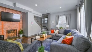 Ein modernes Wohnzimmer mit Kamin, grauen Sofas, einem Couchtisch und einer Treppe, die in einen oberen Bereich führt.