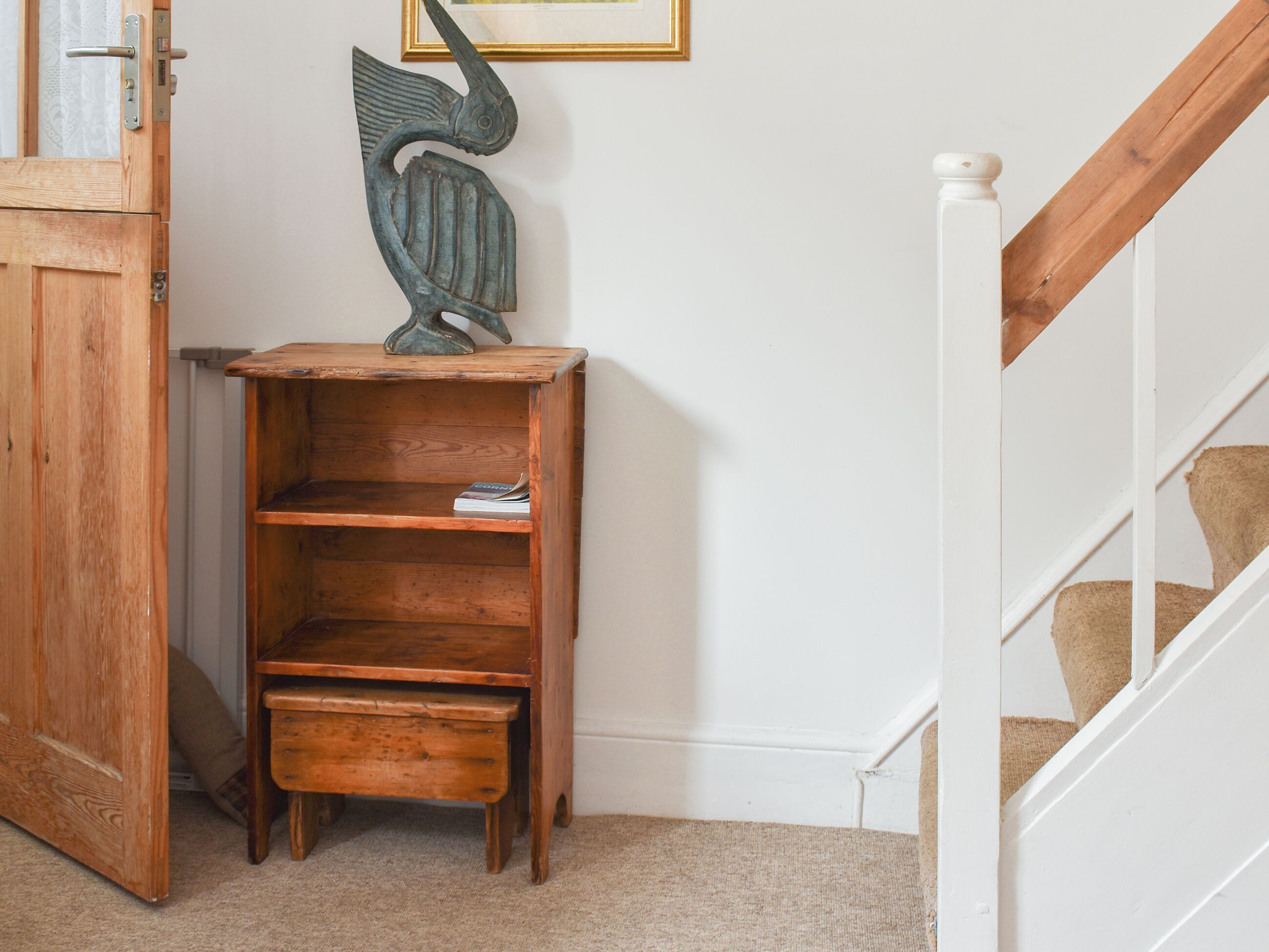 A corner of a room with a wooden bookshelf, a white wall, and a white staircase.