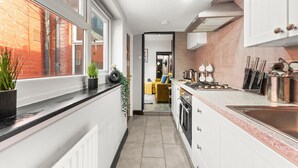 Una cocina estrecha con ventana, una vista de un sofá amarillo y una pared de ladrillo afuera.