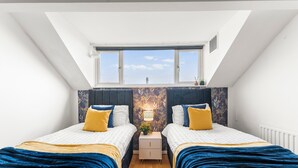 Un dormitorio con dos camas, un tragaluz, una mesita de noche con lámpara y vistas al cielo.