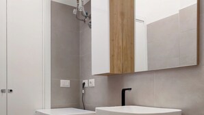 A modern bathroom with a built-in washing machine, a wooden vanity with a white sink, and a mirror above the vanity. - OXILIA (Milan)