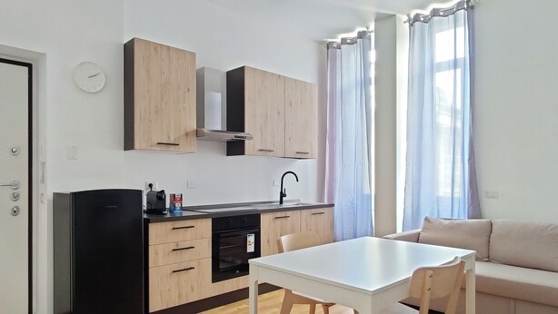 A modern kitchen with wooden cabinets, a black refrigerator, and a white dining table with chairs. - OXILIA (Milan)