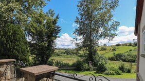 A balcony with a stone bench, a wrought iron railing, and a view of rolling green hills and trees. - Hillside Lodge (Llandrindod Wells)