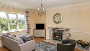 A living room with a sofa, ottoman, fireplace, television, and a view of the outdoors. - Hillside Lodge (Llandrindod Wells)