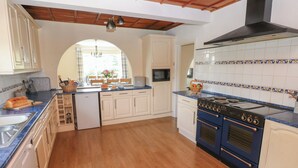 A kitchen with wooden flooring, white cabinets, a blue stove, and a tiled backsplash. - Hillside Lodge (Llandrindod Wells)