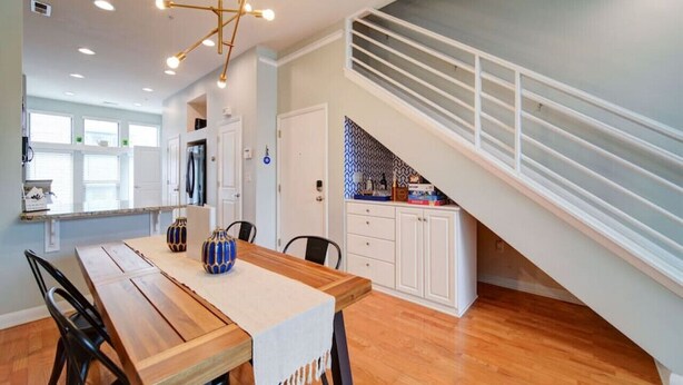 A modern kitchen with white cabinets, a wooden dining table, and a staircase with white railings. - `The Nest`—South End—Rooftop Terrace—Light Rail! (Charlotte)