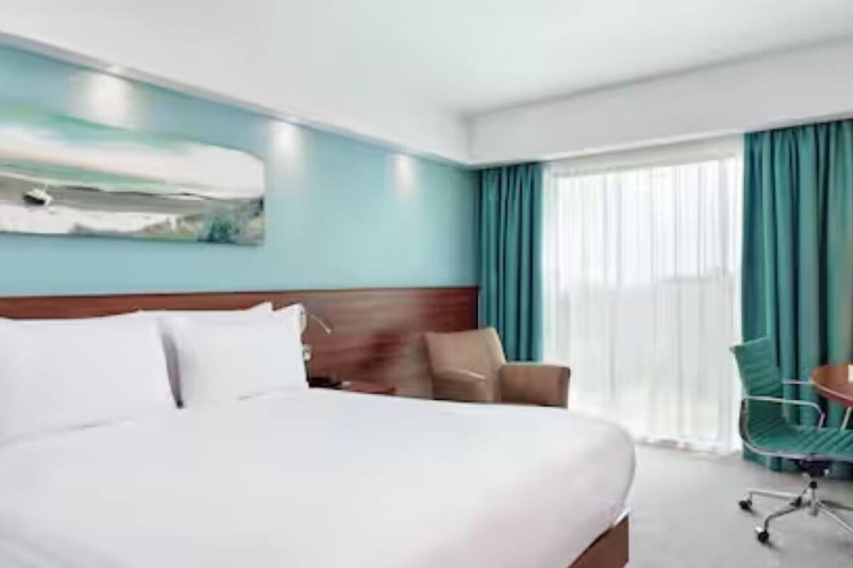 Habitación de hotel con una cama grande, cabecera de madera, un escritorio con silla y una ventana con cortinas.