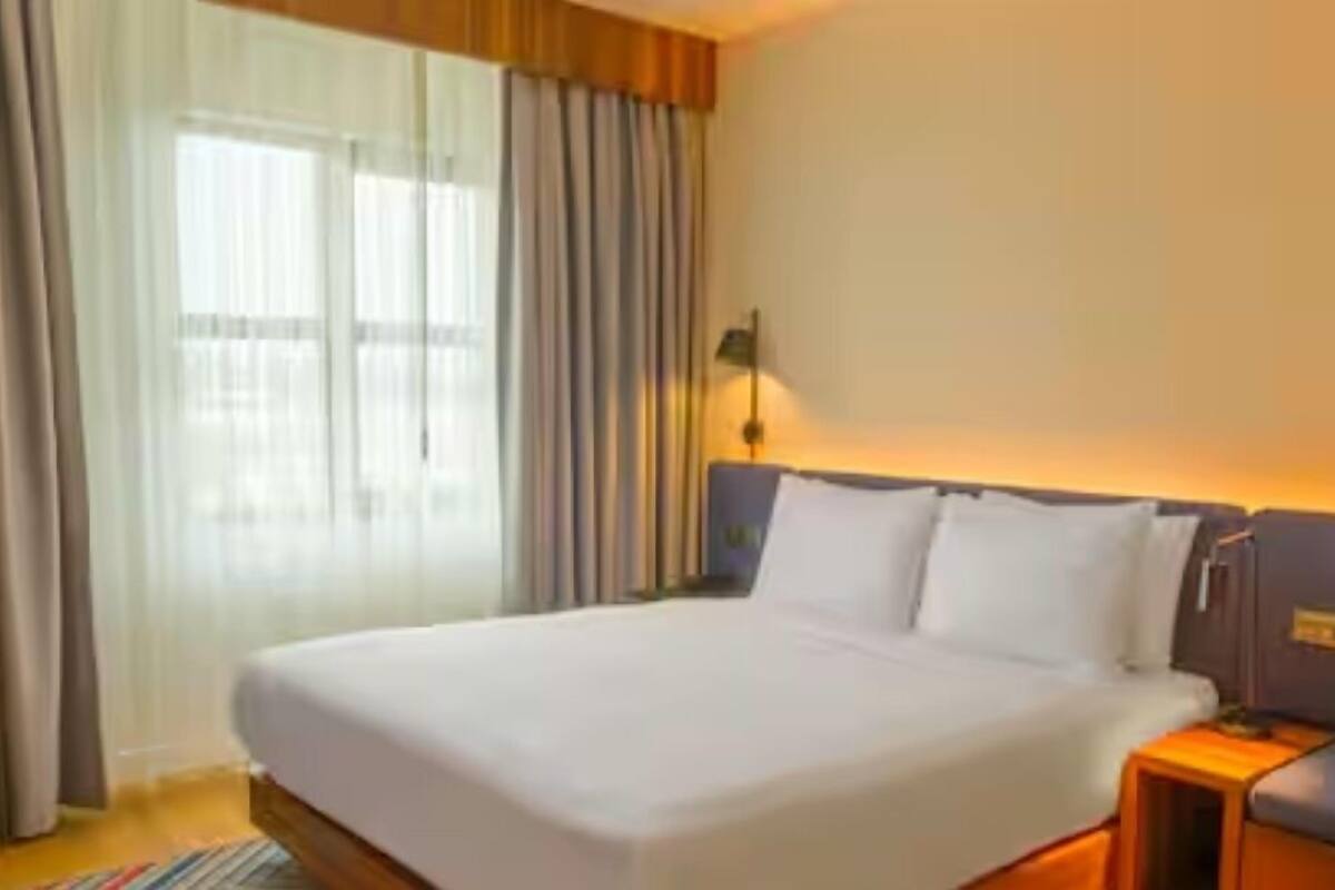 Una habitación de hotel con una cama grande, una mesita de noche, una lámpara y una ventana con cortinas.