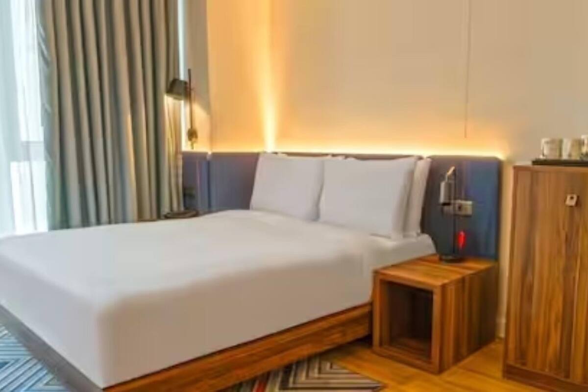 Una habitación de hotel con una cama, una mesita de noche, un armario de madera y una lámpara.