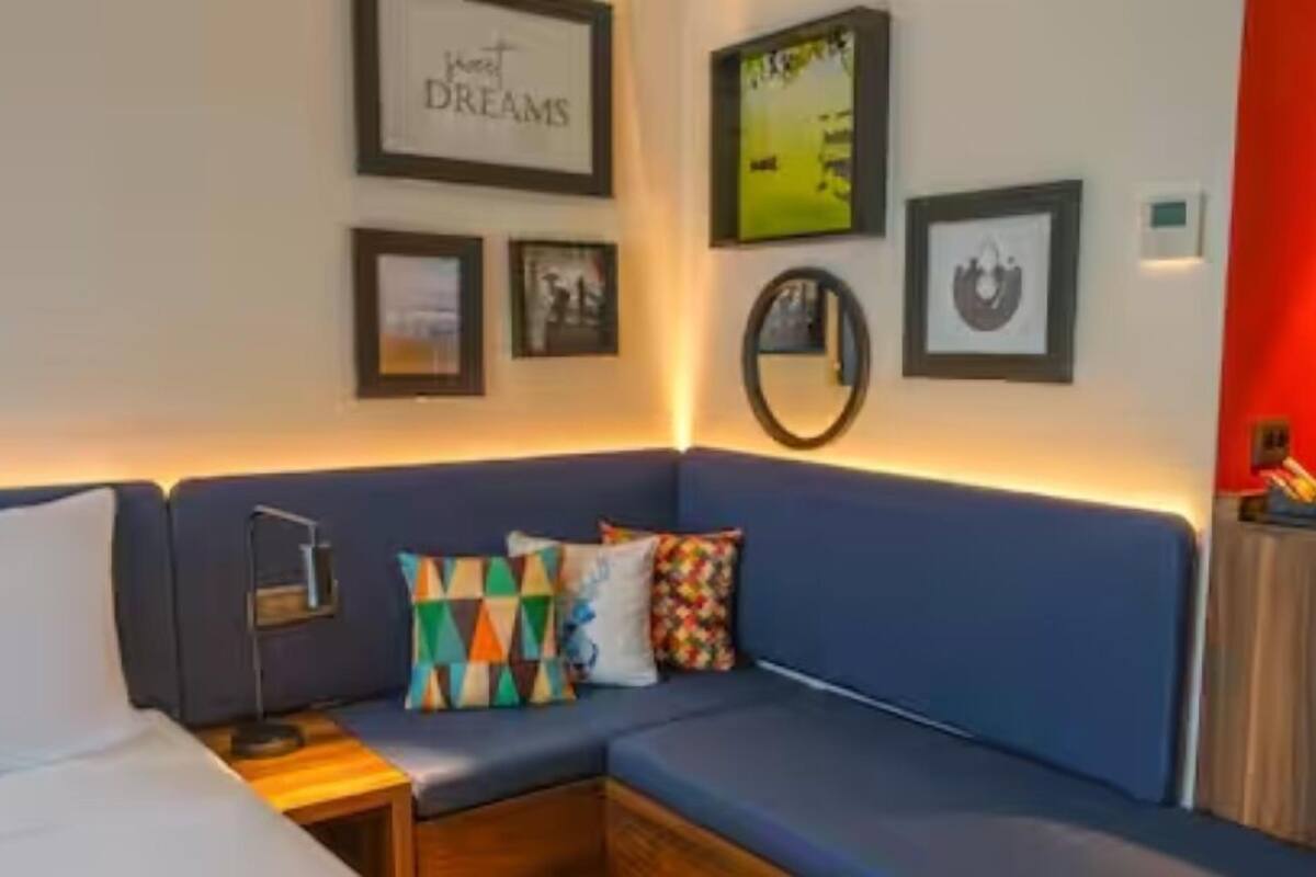 Una habitación moderna con un sofá azul, una pequeña mesa de madera y una lámpara. Varias fotografías enmarcadas adornan la pared.