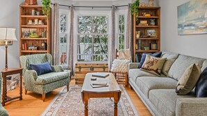 A cozy living room with a green armchair, a grey sofa, and a wooden coffee table. There are books, a lamp, and a painting on the walls. - Lake Front Cottage with Amazing Firepit, Private Dock, Sleeps 6 (Chippewa Falls)