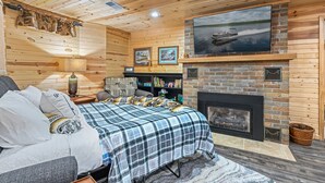 A cozy cabin room with a bed, a fireplace, a TV mounted above it, and a bookshelf. - Lake Front Cottage with Amazing Firepit, Private Dock, Sleeps 6 (Chippewa Falls)