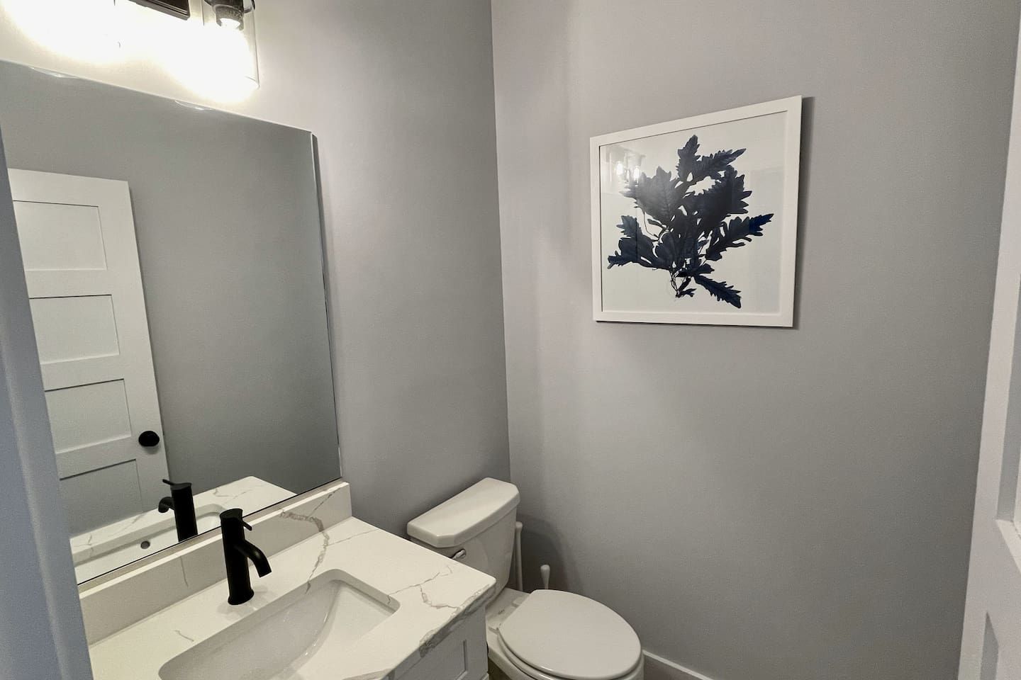A bathroom with a white toilet, a sink with a marble countertop, and a wall-mounted mirror.