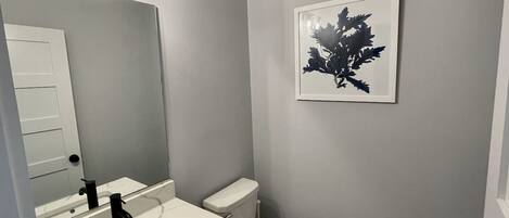 A bathroom with a white toilet, a sink with a marble countertop, and a wall-mounted mirror.
