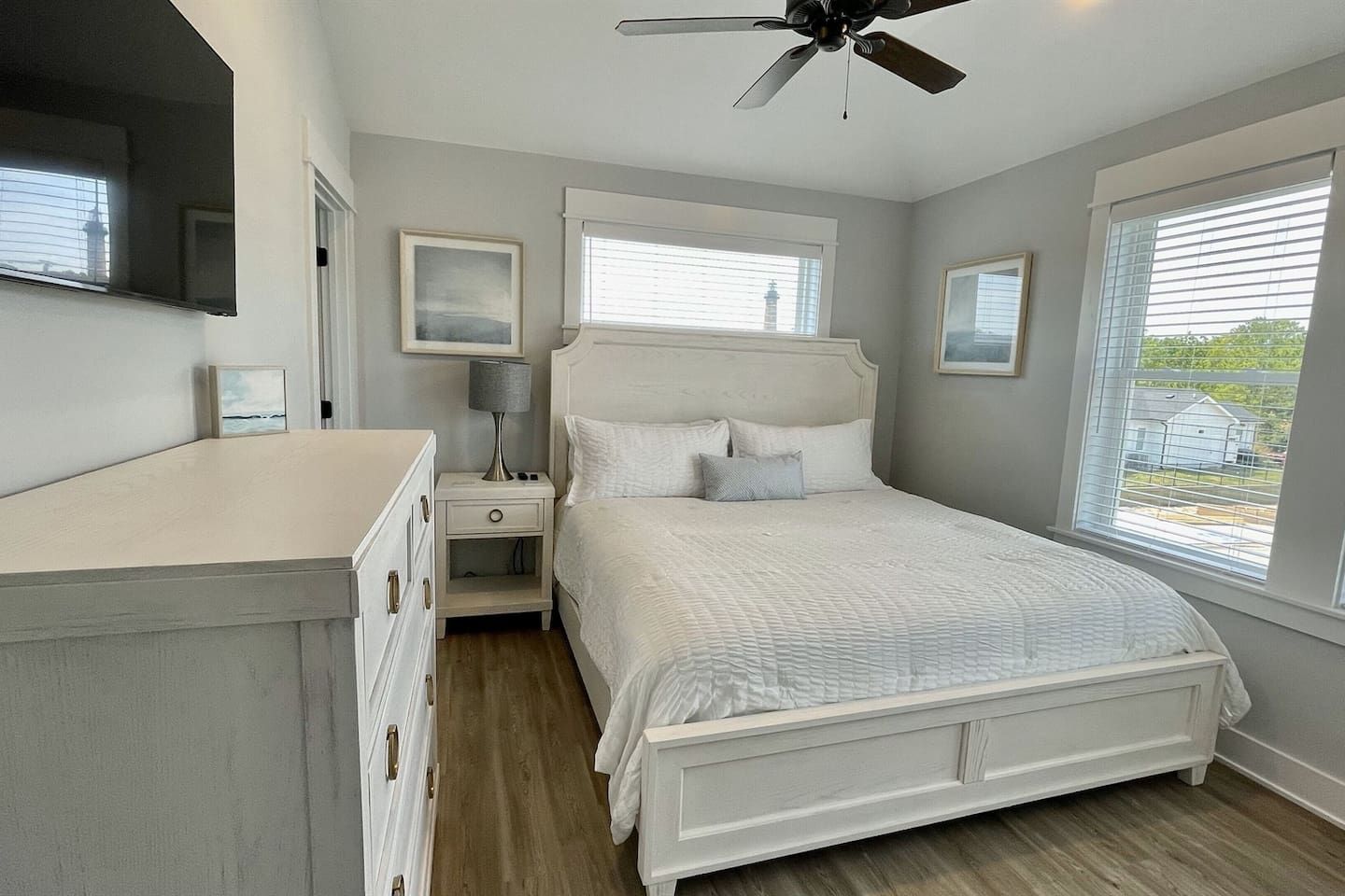 A bedroom with a bed, nightstands, a dresser, a ceiling fan, and windows.