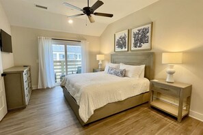 Une chambre à coucher avec un lit, des tables de chevet, un ventilateur de plafond et des œuvres d’art accrochées au mur.