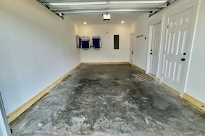 Een smalle gang met een betonnen vloer, witte wanden en een deur aan de rechterkant.