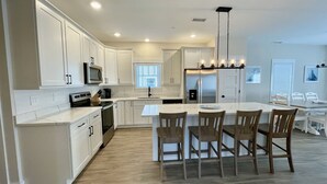 A modern kitchen with white cabinetry, a central island with chairs, a built-in microwave, and a stainless steel refrigerator. - Enjoy The Ocean Breeze just Steps from the Beach! (Corolla)