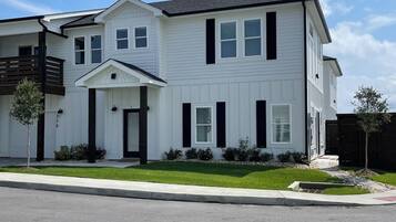 A two-story residential building with a front porch, a garage, and a well-maintained lawn.