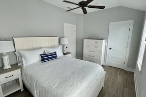 A bedroom with a bed, nightstands, a dresser, a ceiling fan, and a door.