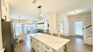 A spacious kitchen with a large island, white cabinetry, and pendant lighting. - Enjoy The Ocean Breeze just Steps from the Beach! (Corolla)