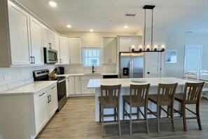 Une cuisine moderne avec des meubles blancs, un îlot central doté de tabourets de bar, un réfrigérateur en acier inoxydable et un four à micro-ondes.