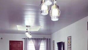 A modern living room with a dark leather sofa, a glass-top coffee table, and a kitchen area with a dark countertop and cabinets. - Grace’s Cozy Place Unit A in Makeni, Lusaka (Lusaka)