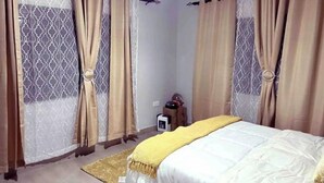 A bedroom with a bed, curtains, a small table, and a rug. - Grace’s Cozy Place Unit A in Makeni, Lusaka (Lusaka)