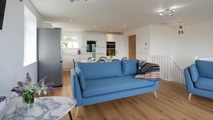 A modern living room with a blue sofa, a marble table, and a vase of flowers. - Treen (St Ives)