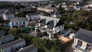 A modern two-story house with a balcony, surrounded by other houses and greenery. - Treen (St Ives)