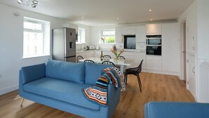 A modern kitchen with white cabinets, a dining table, and a blue sofa. - Treen (St Ives)