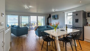 A modern living space with a dining area, a sofa, and a view of the sea. - Treen (St Ives)