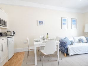A compact living space with a kitchenette, a dining table with chairs, a bed with a blue patterned cover, and two framed pictures on the wall. - Sublyme (Lyme Regis)