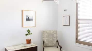 Une chambre à coucher comprenant un lit, une chaise, une commode, un lustre et une fenêtre avec des stores.