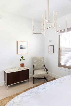 A bedroom with a bed, a chair, a dresser, a chandelier, and a window with blinds. - NEW urban cottage, The Vine & Round Top! (Austin County)
