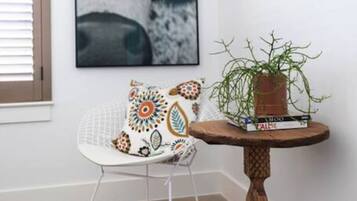 Une pièce d’angle avec une chaise blanche, une table ronde en bois ornée d’une plante, et une photographie en noir et blanc accrochée au mur.