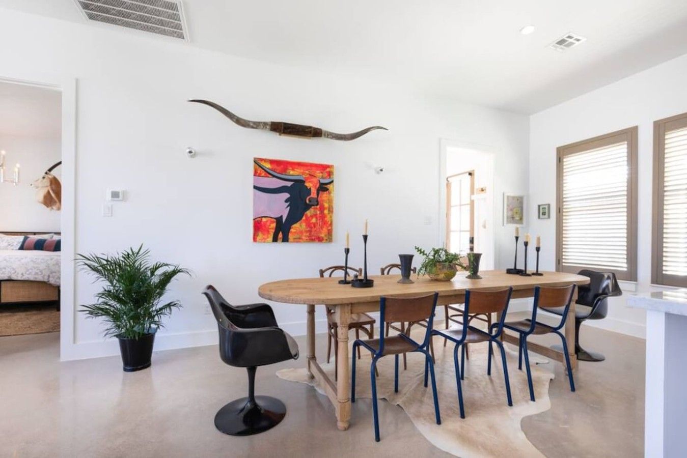 Een eethoek met een ronde tafel, stoelen en een schilderij aan de muur.