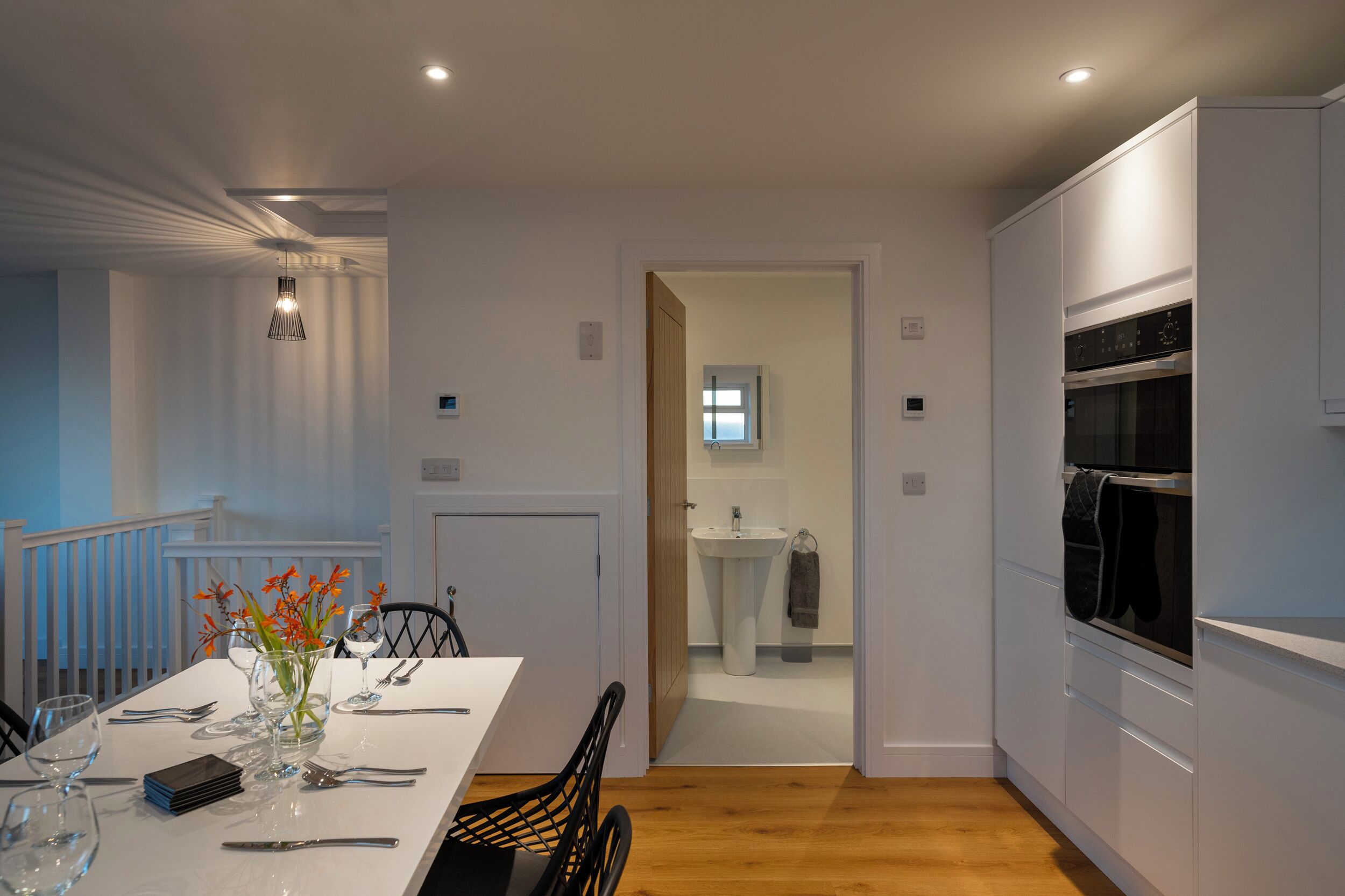 A modern kitchen with white cabinets, a built-in oven, and a dining area with a table set for two.