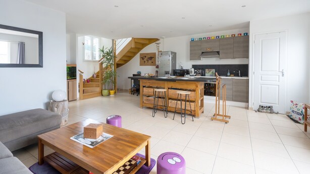 Una sala de estar moderna con una mesa de centro de madera, un sofá gris y una cocina con una escalera de madera.