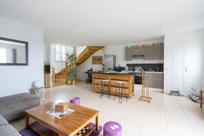 A modern living room with a wooden coffee table, a grey sofa, and a kitchen area with a wooden staircase.