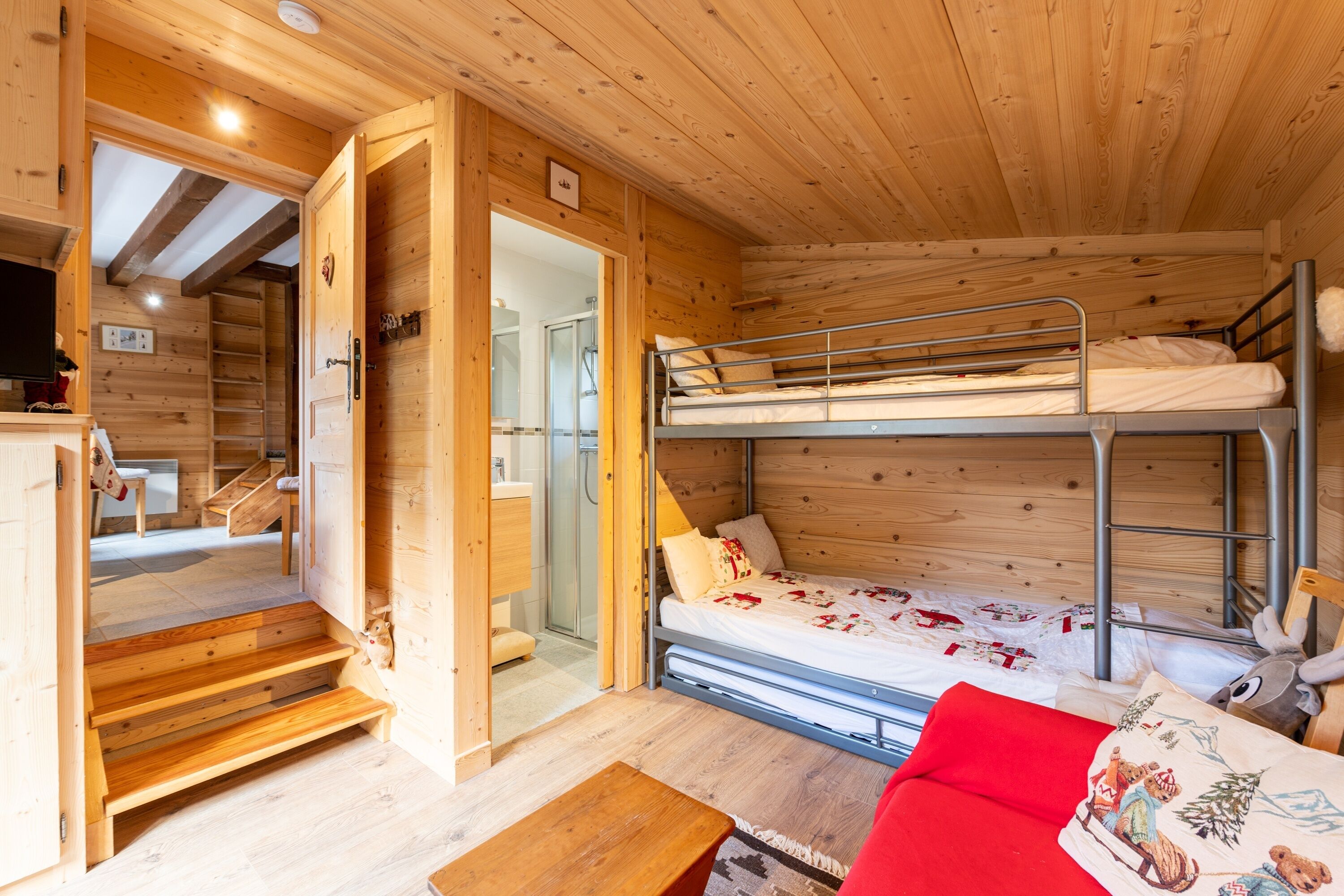 L’intérieur d’une cabane en bois, avec un lit superposé, une petite table et un canapé rouge.