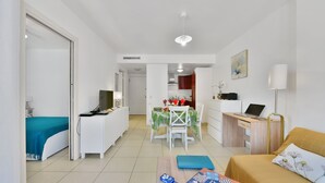 Una habitación de hotel moderna con una cama, un escritorio, una silla, una mesa de comedor con sillas, una lámpara y un cuadro en la pared.